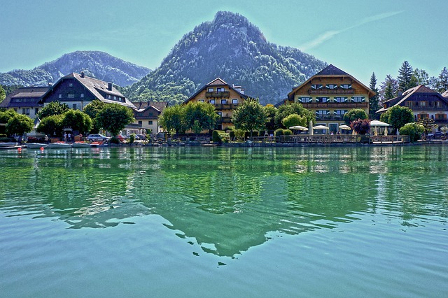 lago con riflesso di case affacciate di fronte con alberi e montagne