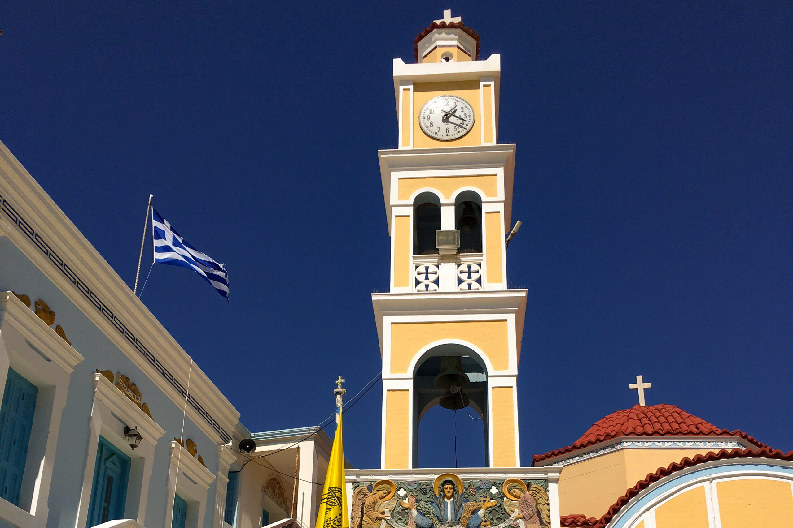 campanile di colore giallo di una piccola chiesa con una bandiera della grecia che sventola